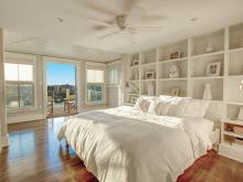 white on white bedroom with built in bookcase wall and water views off adjoining porch